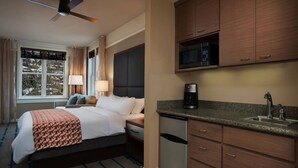 Ein Hotelzimmer mit Bett, Nachttisch, Lampe und einer Mikrowelle in der Küchenzeile.