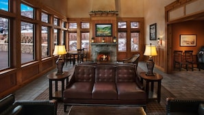 Ein gemütliches Lodge-Interieur mit Kamin, Ledersofa und großen Fenstern mit Blick auf eine verschneite Landschaft.