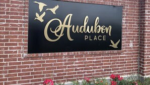 Letrero de Audubon Place con fondo negro y letras doradas.