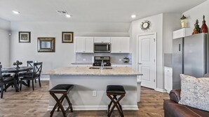 Una cocina moderna con armarios blancos, una isla central y un comedor con mesa y sillas.