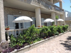 Guests can enjoy shaded seating under umbrellas in the hotel's outdoor area, surrounded by lush greenery and a brick facade with white shutters.