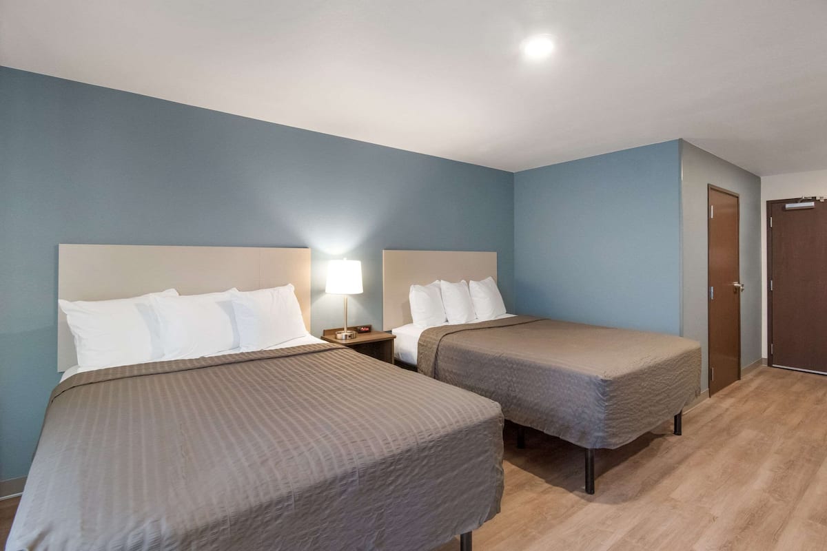 A hotel room with two single beds, a nightstand with a lamp, and a wooden floor.