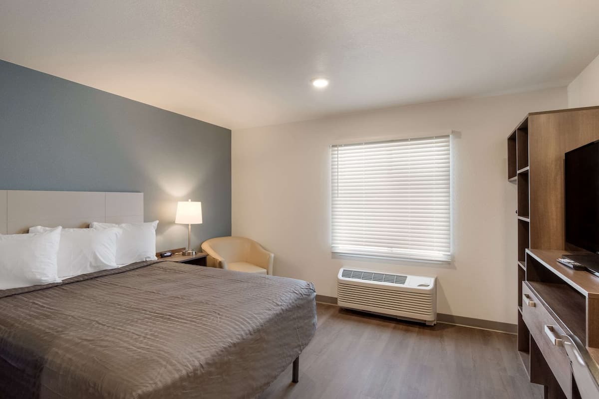 A hotel room with a bed, a chair, a desk, a TV, and a window with blinds.