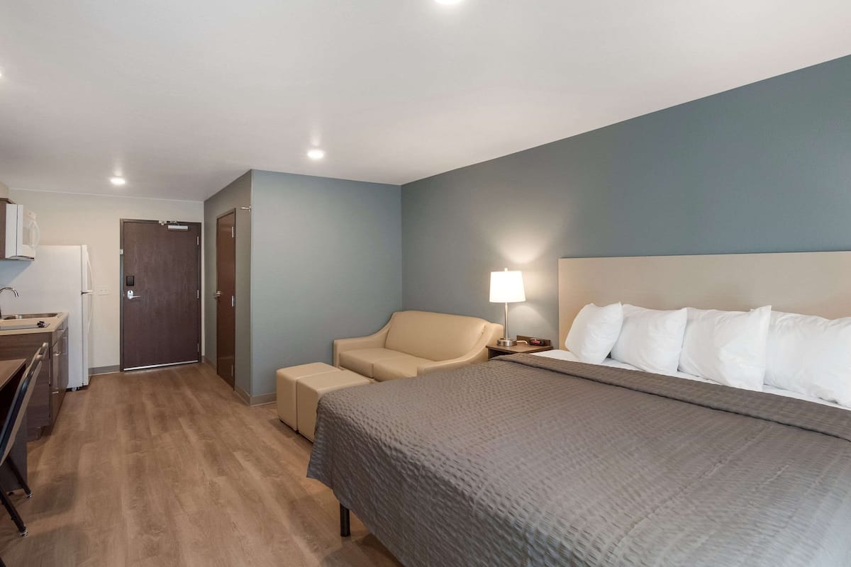 A hotel room with a bed, a desk with a chair, a sofa, and a lamp.
