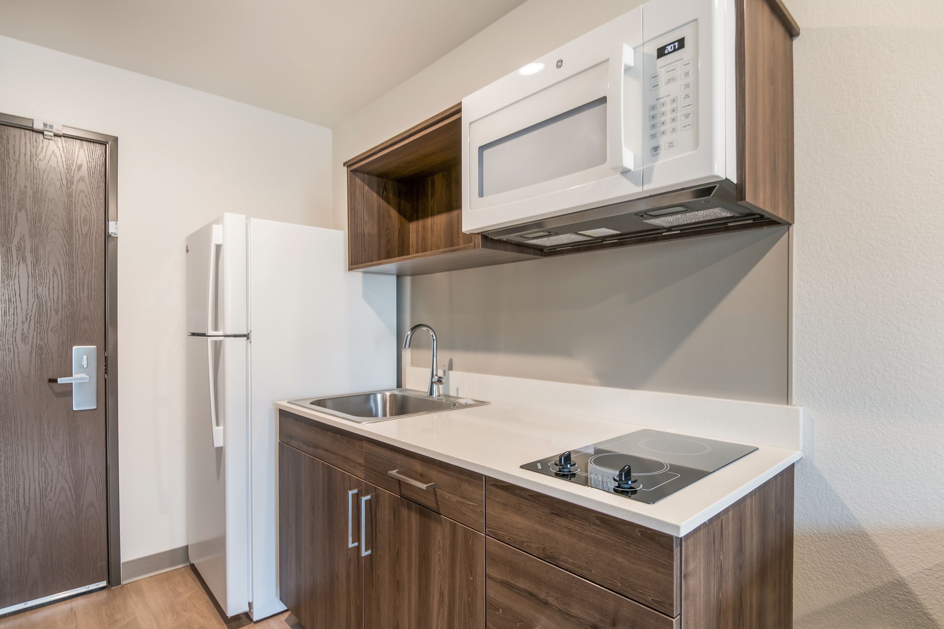 A compact kitchen with a built-in microwave, a sink, and wooden cabinets.