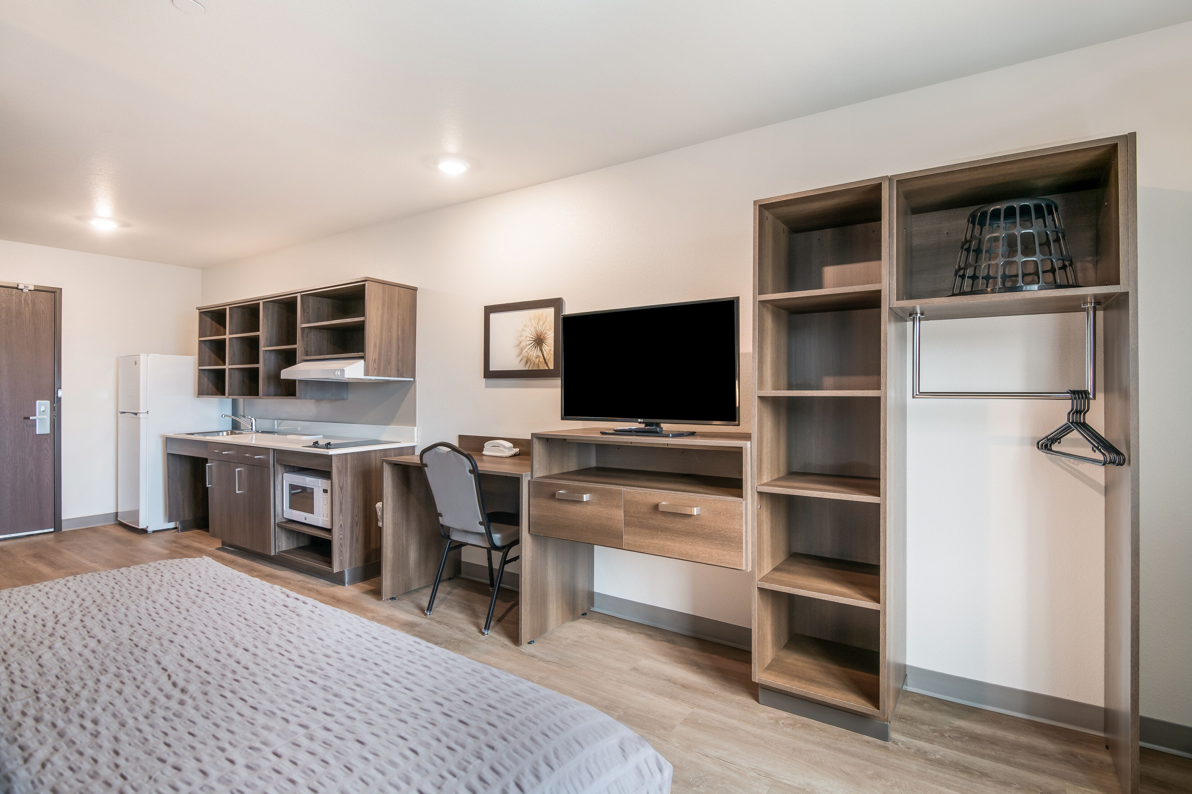 Un dormitorio moderno con cama, escritorio con ordenador, silla y estanterías empotradas.