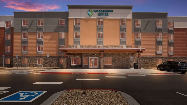Un hôtel à plusieurs étages, doté d’un toit plat, d’une entrée centrale et d’un espace de stationnement délimité par un panneau indiquant une voie d’accès pour les véhicules d’urgence.