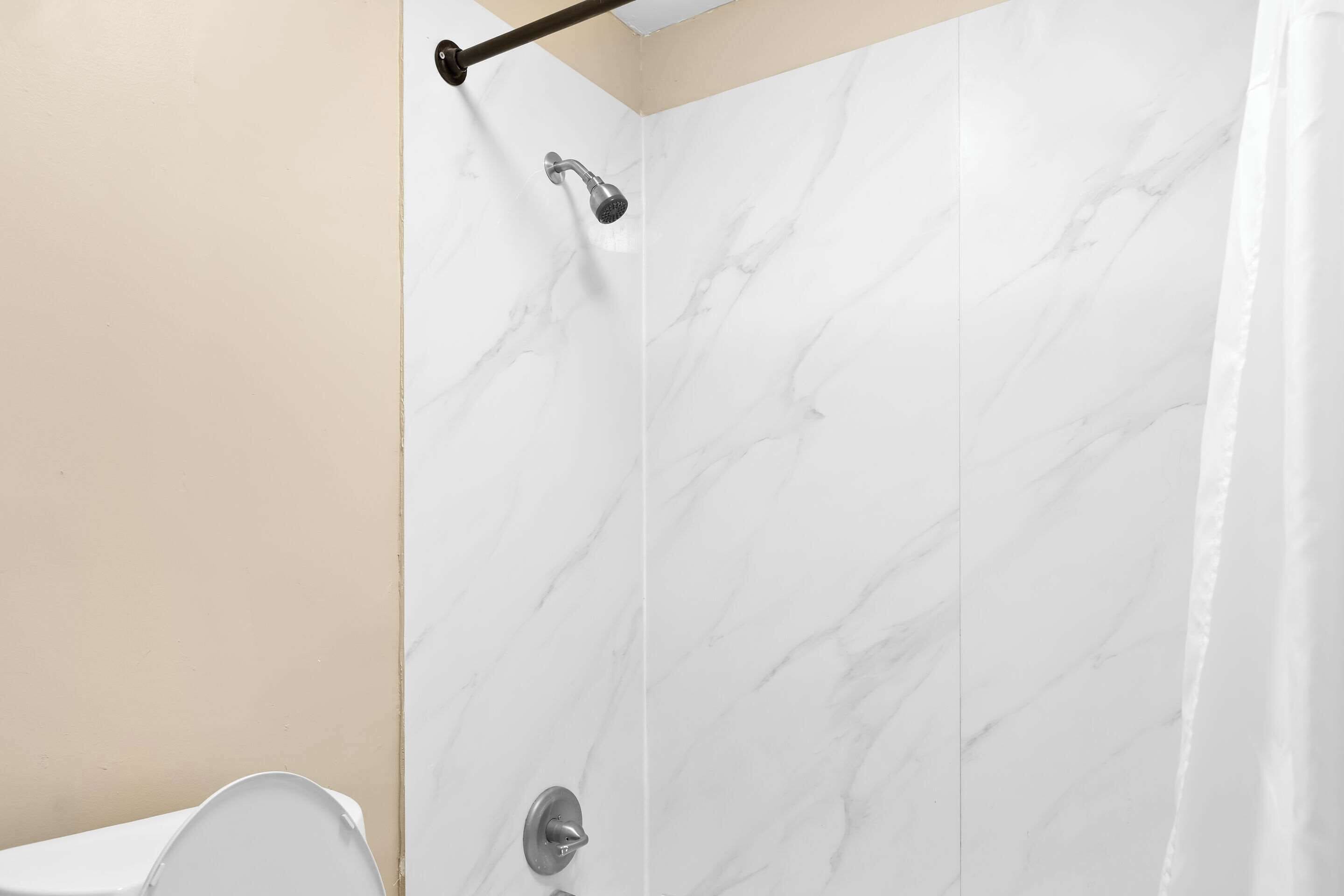 A bathroom with a shower, marble walls, and a beige wall.