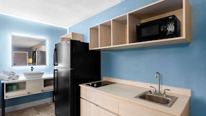 A compact kitchen with a black refrigerator, a built-in microwave, a sink, and a wooden shelf above the microwave. - Suburban Studios Brunswick of I-95 (Brunswick)