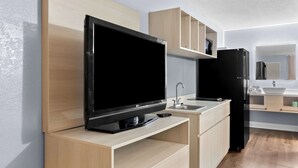 A modern kitchen with a flat-screen TV, wooden cabinets, a black refrigerator, and a built-in sink. - Suburban Studios Brunswick of I-95 (Brunswick)