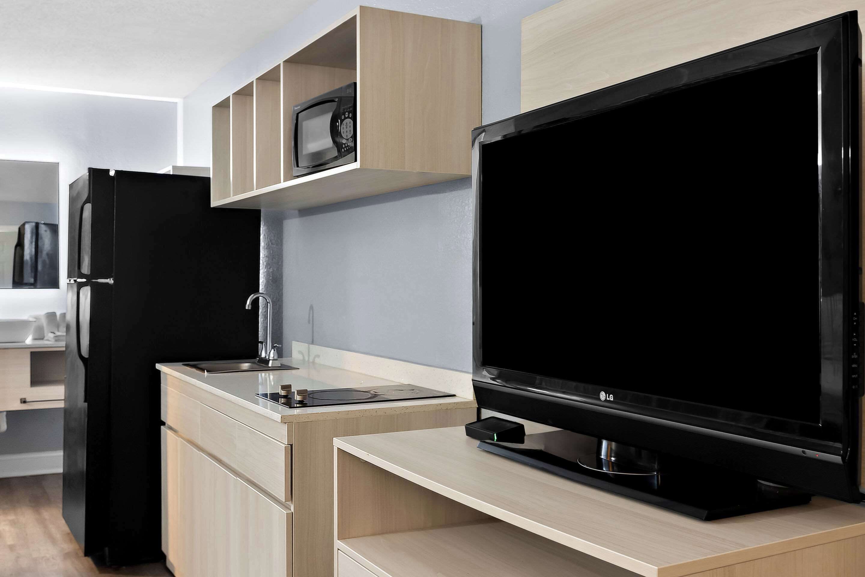 Una cocina moderna con un refrigerador negro, un microondas, un televisor de pantalla plana y alacenas de madera.