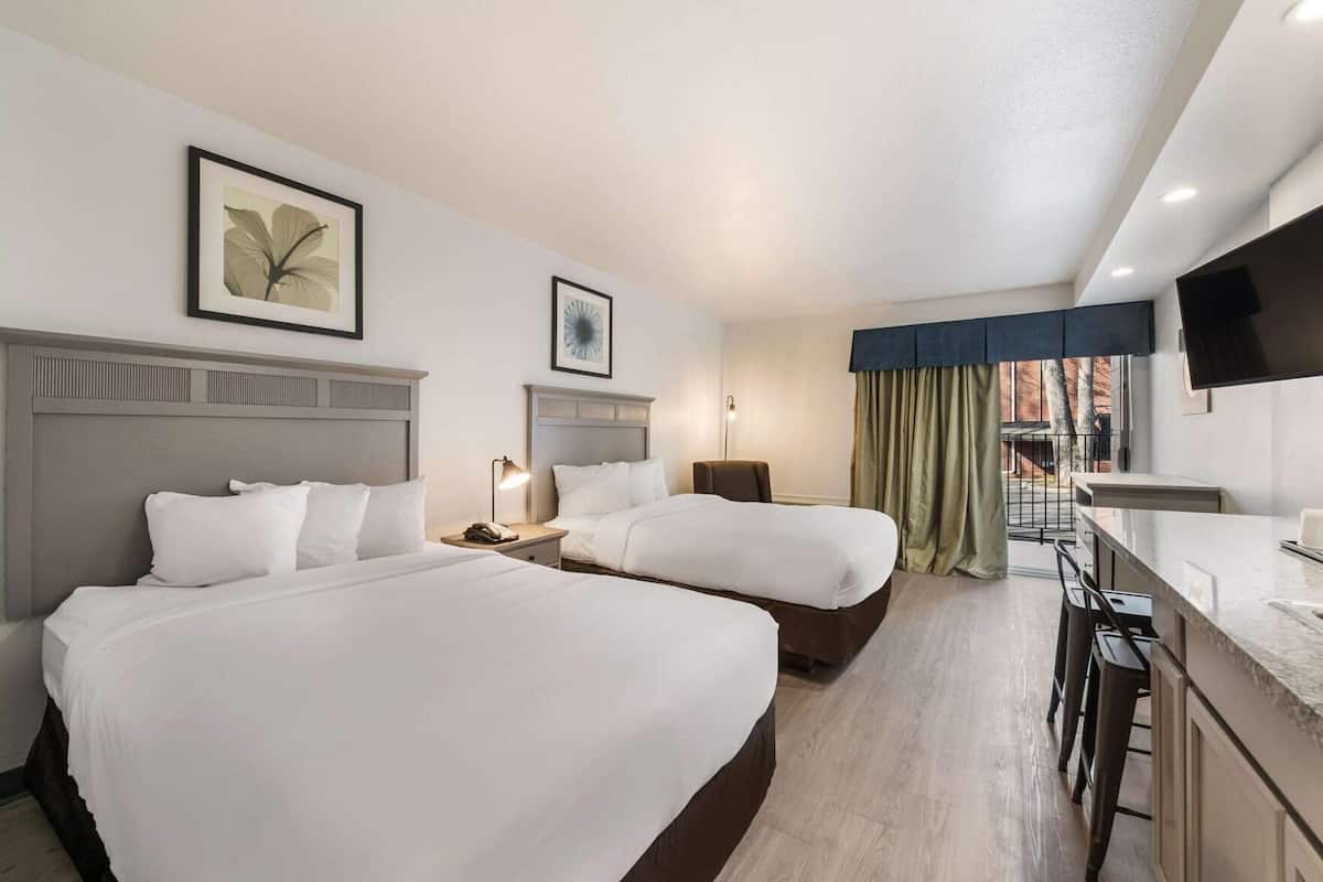 A hotel room with two beds, a desk, a chair, a TV, and a window with curtains.