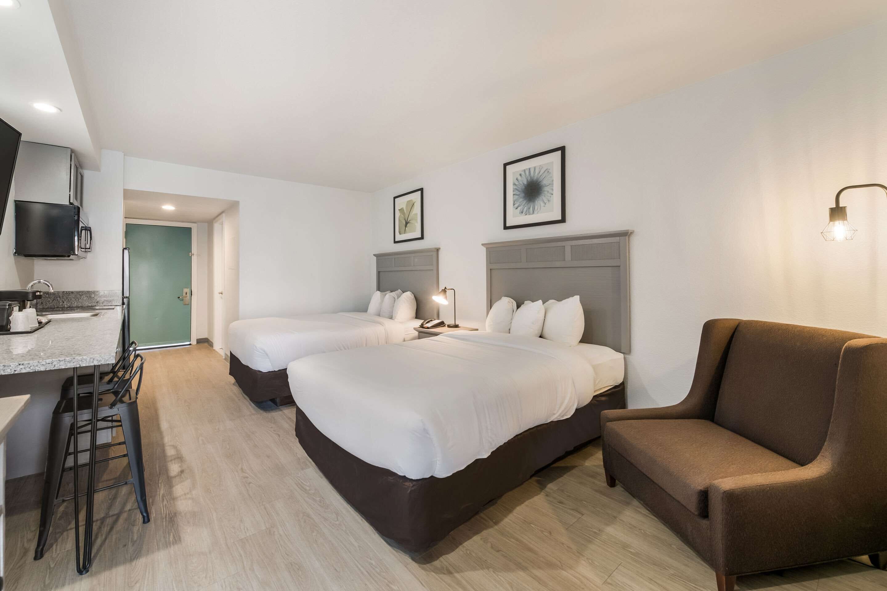 Hotellihuone, jossa on kaksi sänkyä, sohva, työpöytä tuolilla ja televisio.