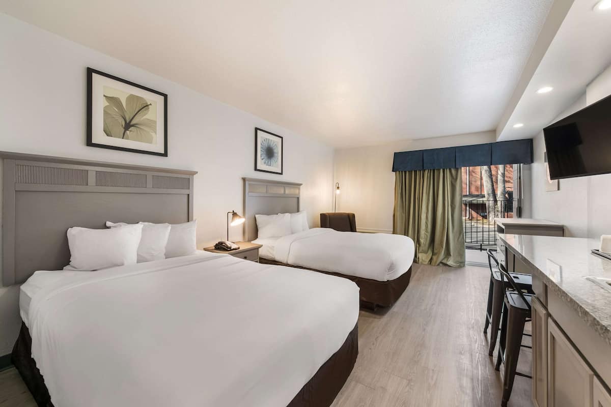 A hotel room with two beds, a desk with a chair, a TV mounted on the wall, and a window with curtains.