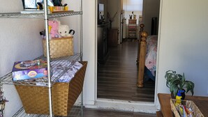 Un couloir dans lequel on trouve un présentoir métallique contenant divers objets, un panier en osier et une table en bois ornée d’une plante et de fleurs.