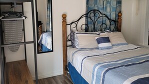 Une chambre à coucher avec un lit, un ventilateur de plafond, une fenêtre avec des rideaux, une étagère avec une plante et un miroir.