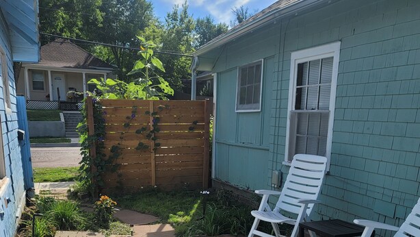 Une terrasse carrelée en pierre, avec des chaises blanches et une clôture en bois.