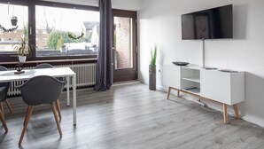 Uma sala de estar moderna com área de jantar, TV na parede e vista para o exterior.