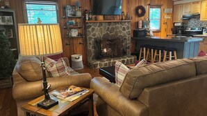 Ein gemütliches Wohnzimmer mit Kamin aus Stein, einer Ledersofa und einem darüber montierten Fernseher.