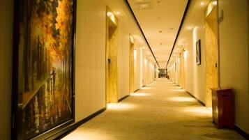 A long, narrow hotel corridor with doors on both sides, a carpeted floor, and a painting on the left wall.