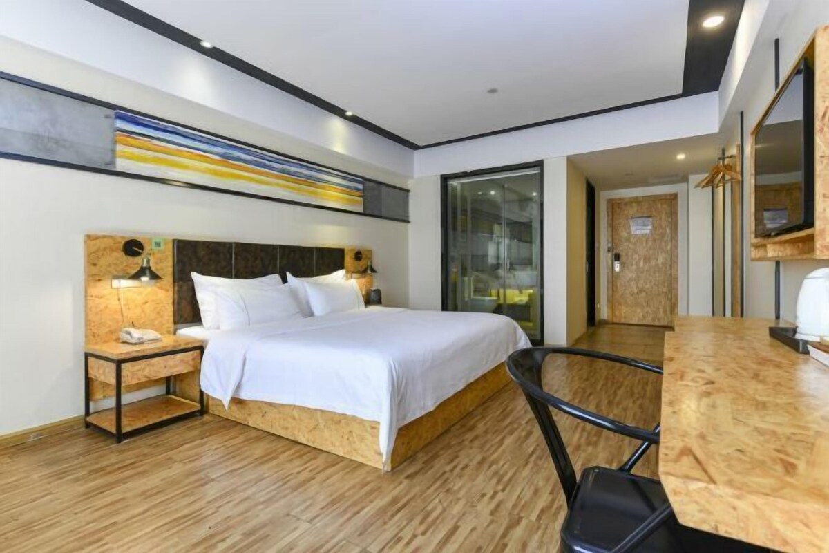 A modern hotel room with a wooden bed, a desk, and a large window.