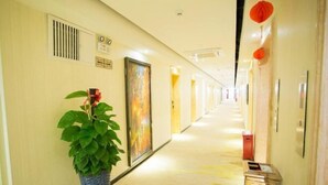 A hotel hallway with a potted plant, a door with a colorful artwork, and a trash bin. - Meet Fashion Hotel (Huidong OCT Store) (Huidong)