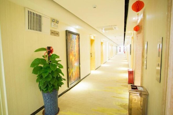 A hotel hallway with a potted plant, a door with a colorful artwork, and a trash bin. - Meet Fashion Hotel (Huidong OCT Store) (Huidong)