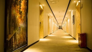 A long, well-lit hallway with a wooden floor and a large painting on the left wall. - Meet Fashion Hotel (Huidong OCT Store) (Huidong)