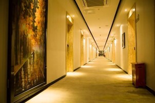 Um corredor longo e bem iluminado, com piso de madeira e uma pintura grande na parede esquerda.