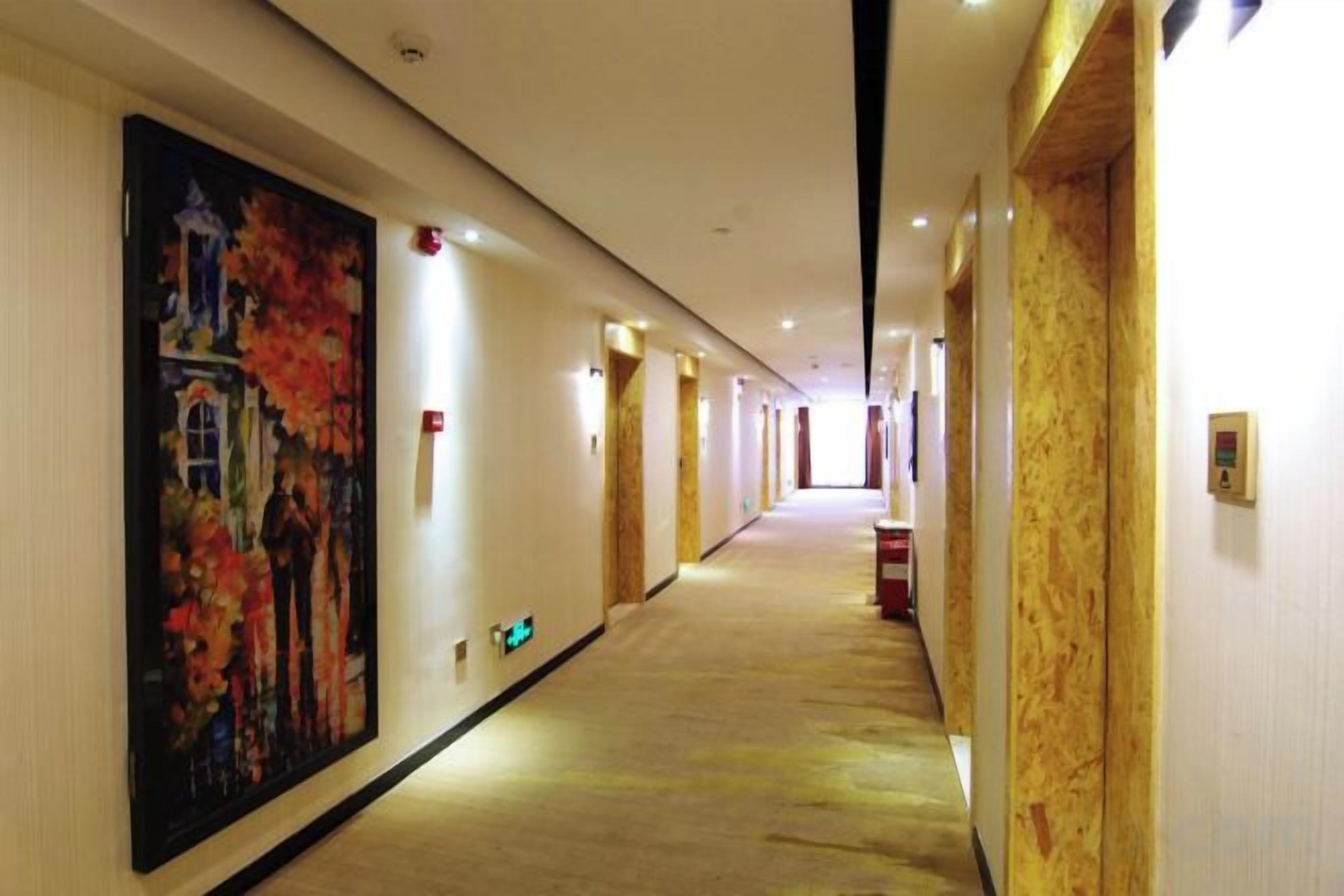 Un corridoio d'hotel con un grande quadro sulla parete sinistra, pavimento rivestito di moquette e porte alla destra.