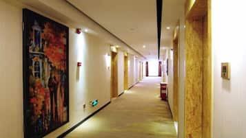 Un corridoio d'hotel con un grande quadro sulla parete sinistra, pavimento rivestito di moquette e porte alla destra.
