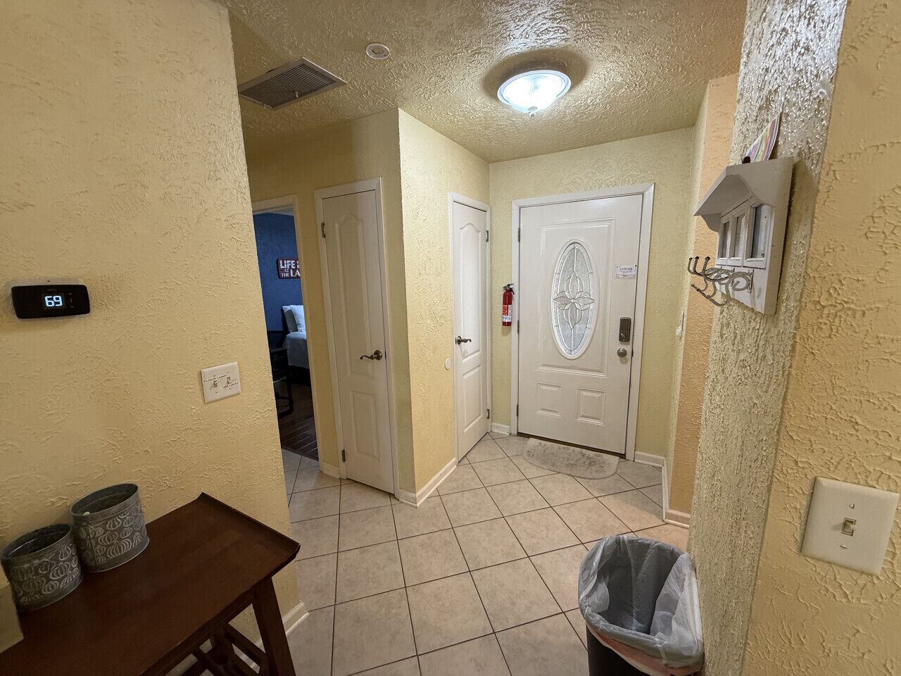 A hallway with beige walls, white doors, a wooden table with two trash bins, and a ceiling light fixture.