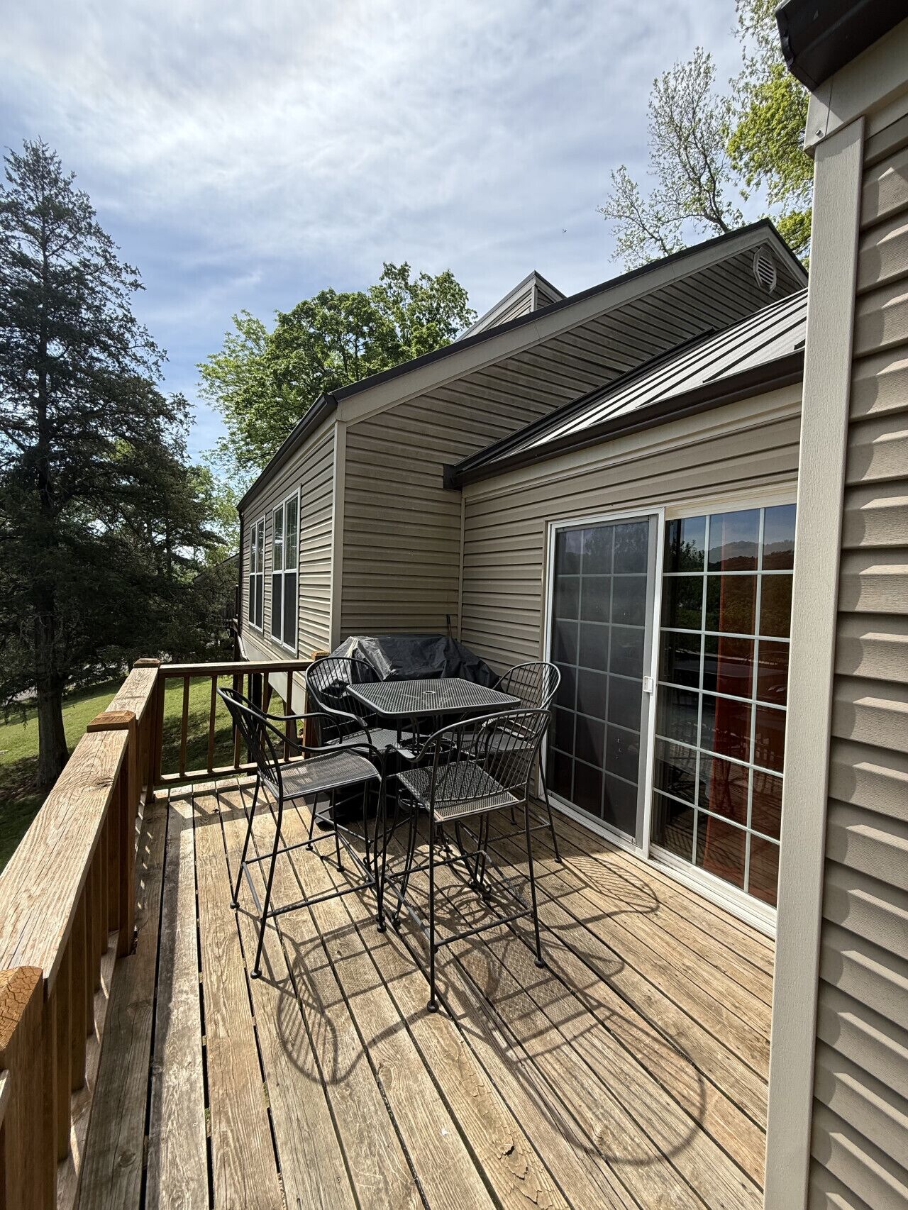 A deck with a metal table and chairs, a wooden railing, and a house with siding and a garage door.