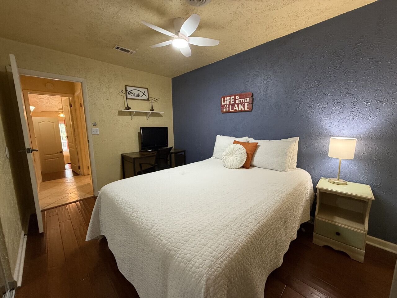 A bedroom with a bed, a nightstand, a lamp, a television, and a door leading to another room.
