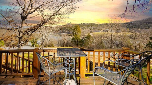 Eine Holzterrasse mit Metallstühlen und einem Tisch, mit Blick auf eine malerische Landschaft aus Bäumen und Hügeln.