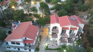 An aerial view of a residential area with two multi-story buildings featuring red-tiled roofs and white walls. - Despina studios and rooms (Ikaria)