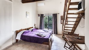 A bedroom with two wooden beds, a balcony with a table, and a TV mounted on a wooden beam. - Despina studios and rooms (Ikaria)