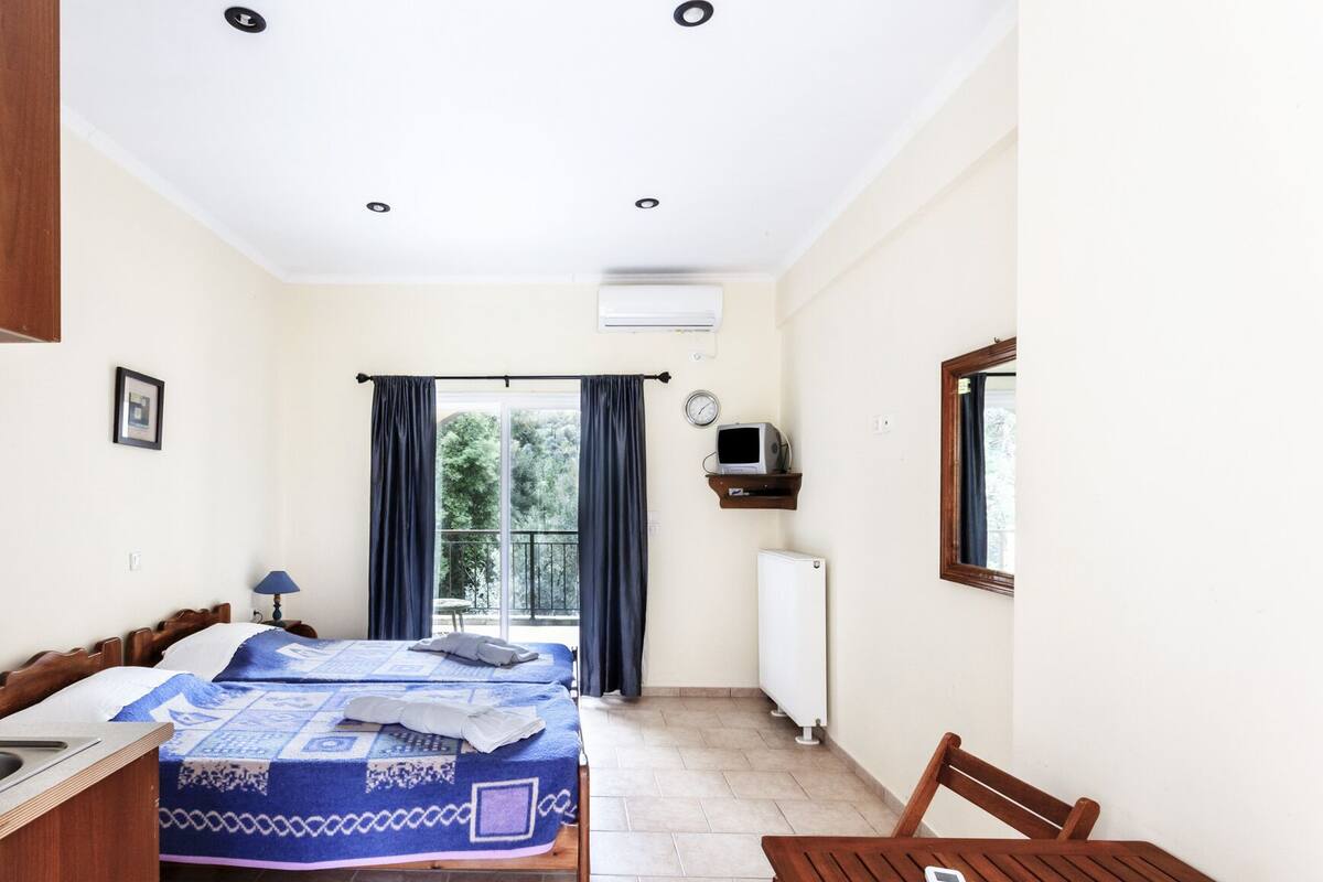 A bedroom with a bed, a table, a chair, a window, and an air conditioning unit.