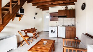 A compact living space with a wooden staircase, a dining area with a table and chairs, a washing machine, a compact kitchen with cabinets and a sink, and a small window. - Despina studios and rooms (Ikaria)