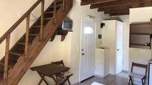 A wooden staircase leading to a room with a white door, a small table, and a chair. - Despina studios and rooms (Ikaria)
