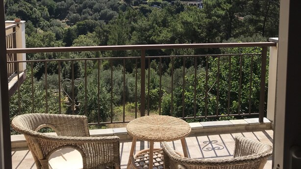 A balcony with wicker furniture and a view of a hilly landscape. - Despina studios and rooms (Ikaria)
