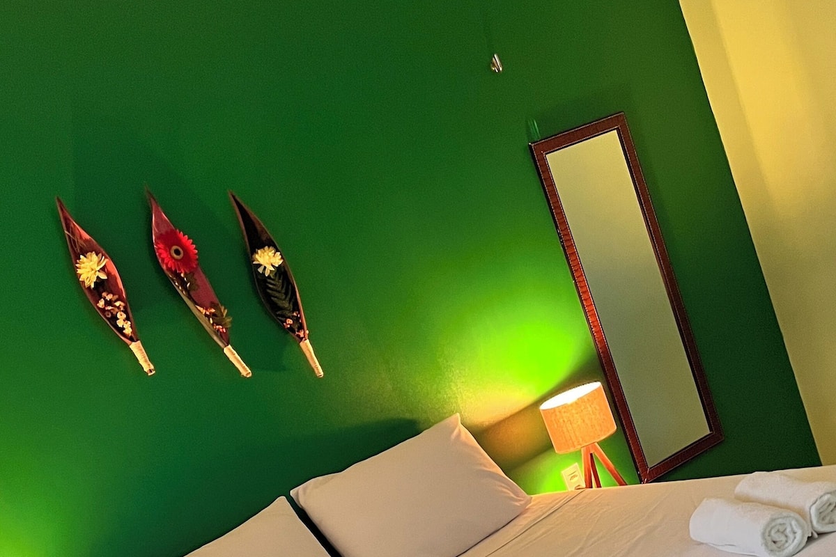 A neatly made bed with white linens, a green wall, and a wooden floor.