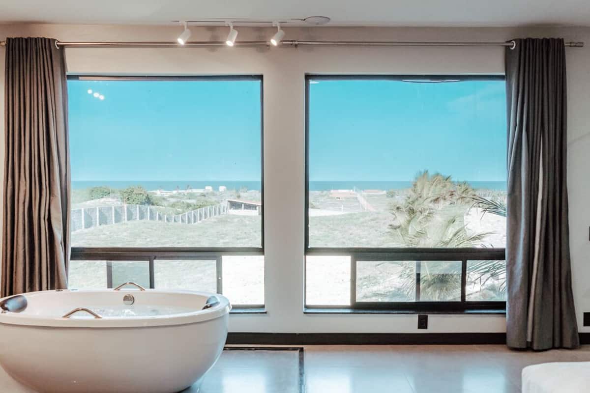 A modern bedroom with a large window, a bathtub, and a bed.