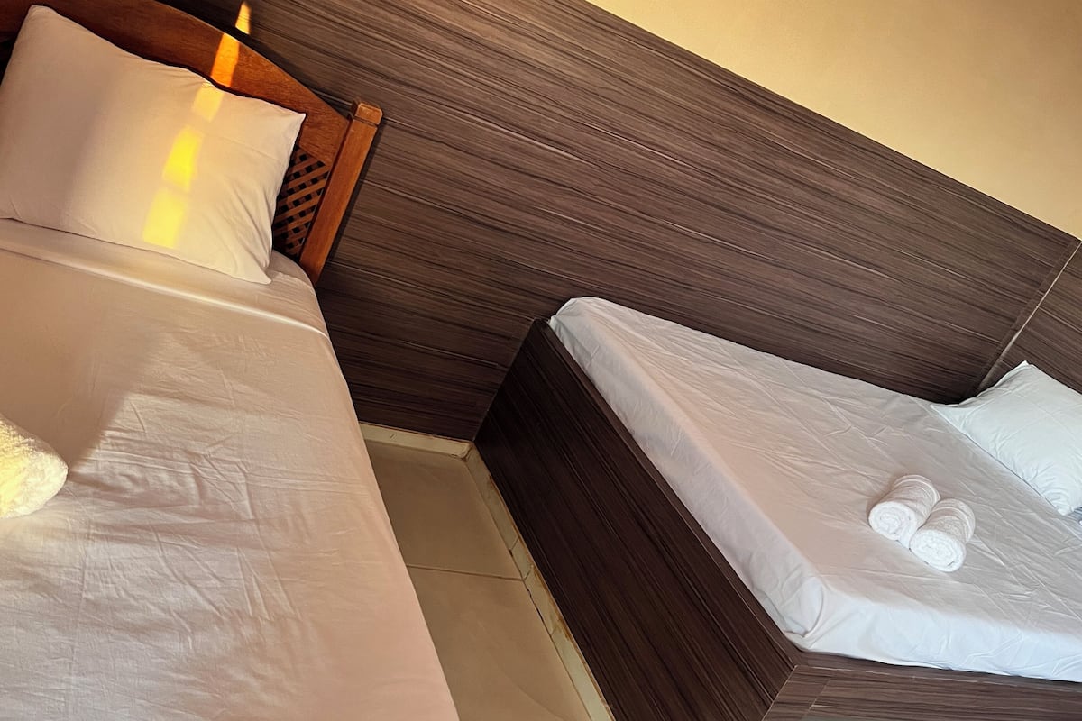Two single beds with wooden headboards and white linens, including towels, in a hotel room.