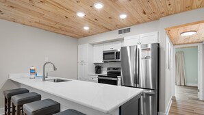 Una cocina moderna con armarios blancos, electrodomésticos de acero inoxidable y techo de madera.