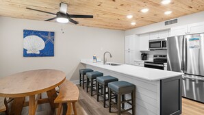 Una cocina moderna con techo de madera, una isla central con taburetes, electrodomésticos de acero inoxidable y una obra de arte azul en la pared.