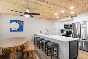 Une cuisine moderne avec un plafond en bois, un îlot central doté de tabourets, des appareils en acier inoxydable et une œuvre d’art bleue accrochée au mur.