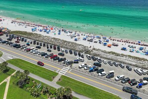 Vue aérienne d’une plage avec un parking et des personnes se baignant ou se promenant sur la plage.