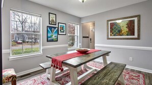 Un coin repas avec une table et des bancs en bois, des œuvres d’art encadrées accrochées aux murs et une vue par la fenêtre.