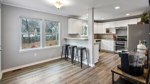 Une cuisine moderne avec des meubles blancs, un îlot central, des tabourets de bar et une grande fenêtre.